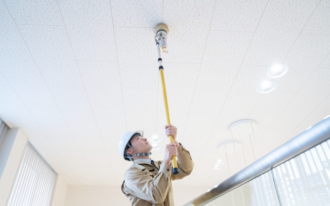 天井に設置された火災報知器を点検する作業員